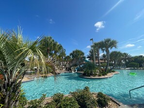 Ein Poolbereich mit Palmen, einer Rutsche und blauem Himmel.