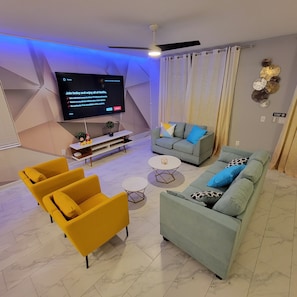 A modern living room with a flat-screen TV, two sofas, a coffee table, and a yellow armchair.