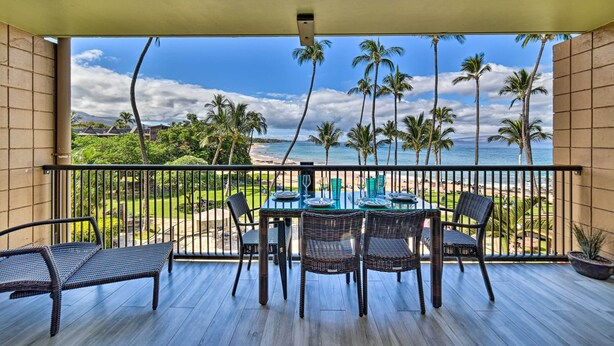 Een balkon met een eettafel, met uitzicht op een strand met palmbomen en een zeegezicht.
