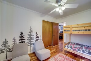 Ein Zimmer mit Etagenbett, einem Sessel, einem Deckenventilator und einer Tür zu einem weiteren Raum.