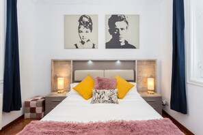 A bedroom with a large bed, two bedside tables with lamps, a headboard, and two wall-mounted artworks.