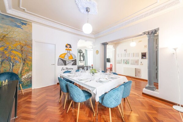 A dining area with a white table set for four, blue chairs, and a painting of a woman on the wall.