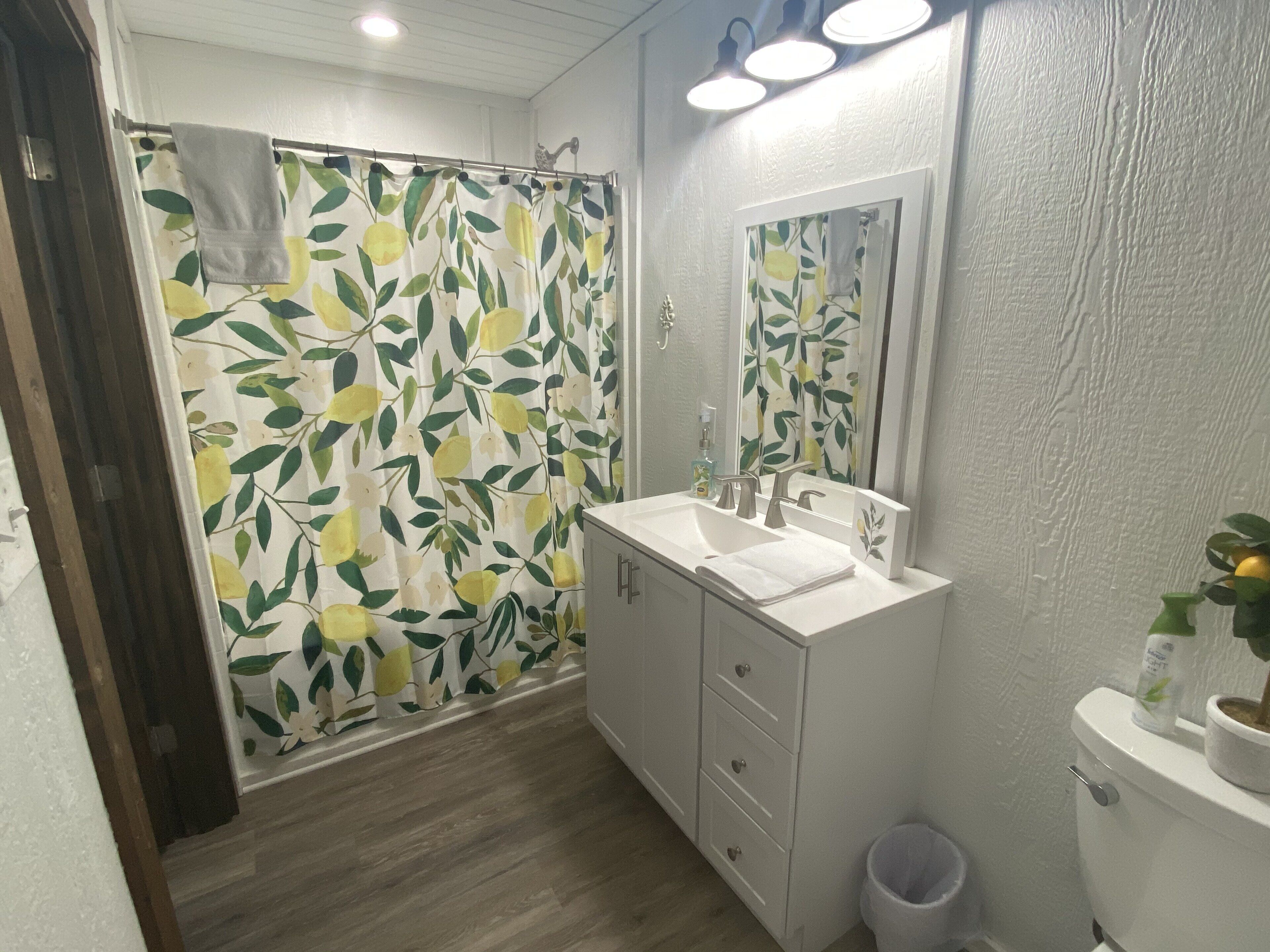 Ein Badezimmer mit Duschvorhang mit floralem Muster, einem weißen Waschbecken, einem Spiegel und einer Toilette.