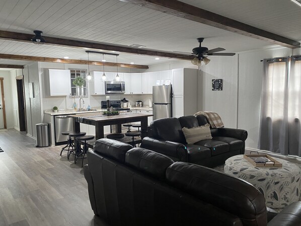 A modern kitchen with white cabinets, a central island, and a dining area with a black leather sofa and ottoman. - Simply Buffalo sleeps 10,  St Joe, AR- Float the middle beautiful Buffalo River (Saint Joe)