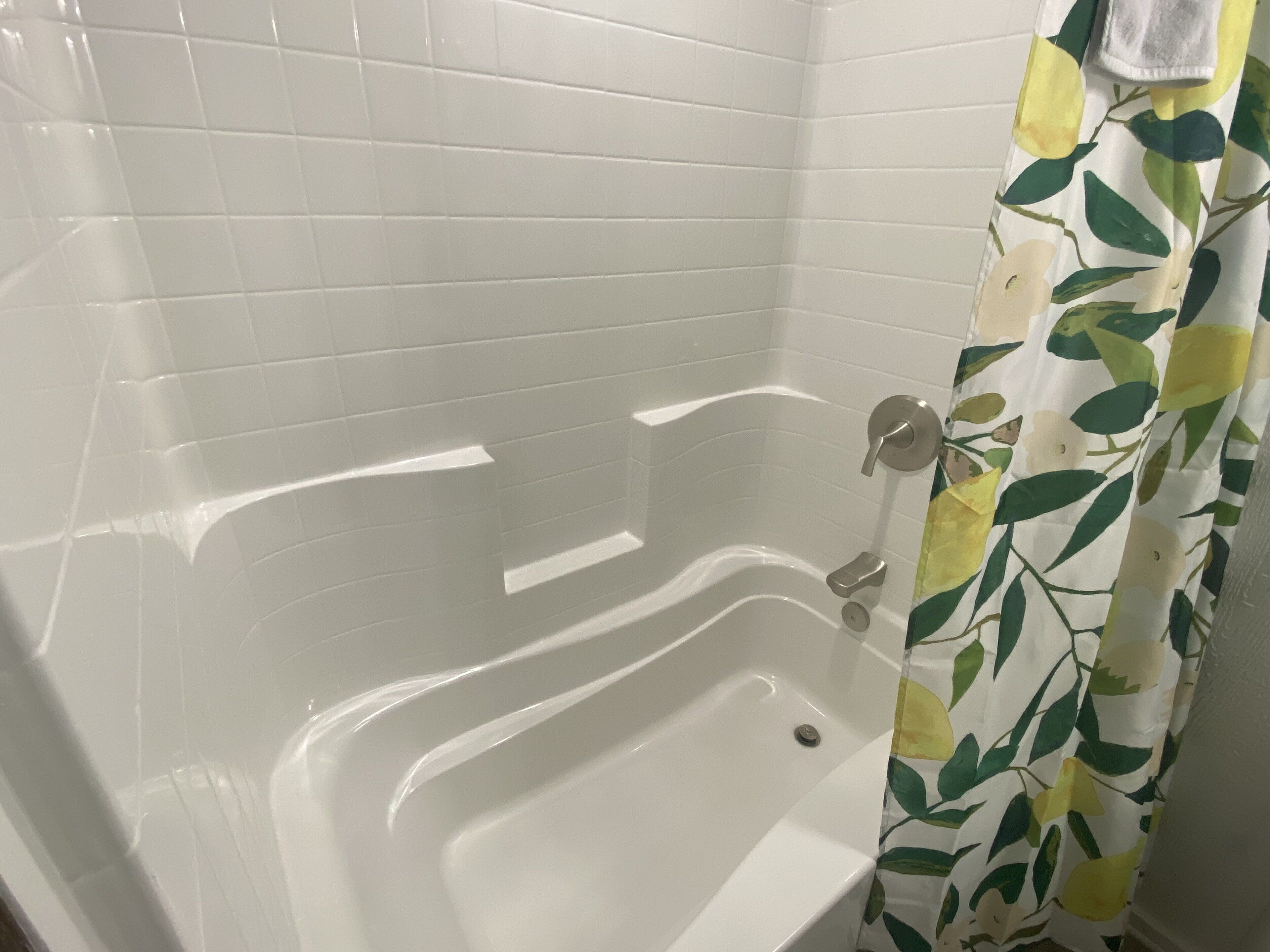 A bathroom with a white bathtub, tiled walls, and a shower curtain with a leaf pattern.