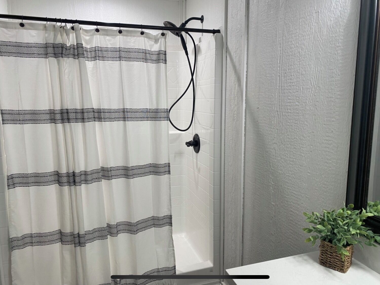 Un baño con cortina de ducha, cabezal de ducha de mano y una planta en maceta sobre una mesita.