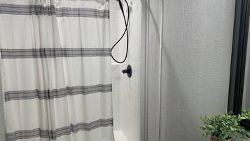 Un baño con cortina de ducha, cabezal de ducha de mano y una planta en maceta sobre una mesita.