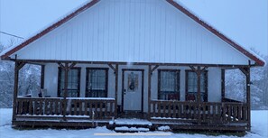 Cozy cabin with a gabled roof and porch, surrounded by a serene winter landscape.