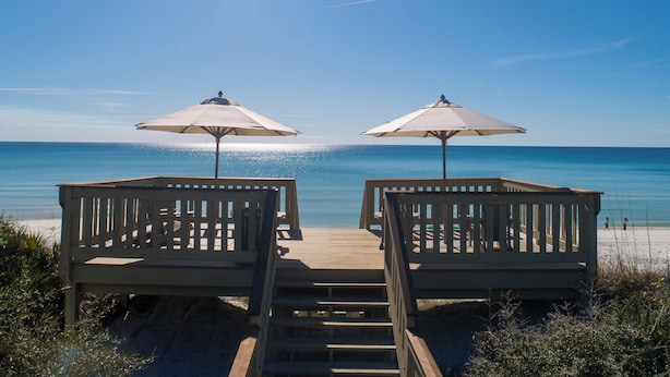 Una terraza de madera con dos sillas de playa y sombrillas, con vista a la playa.