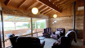 A cozy lounge area with leather sofas and armchairs, a fireplace, and large windows offering a view of the outdoors. - Enjoy Sunrise Views from the comfort of this beautiful home away from home! (Little Grove)