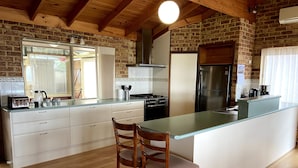 A kitchen with a central island, wooden chairs, a stove, and a refrigerator. - Enjoy Sunrise Views from the comfort of this beautiful home away from home! (Little Grove)