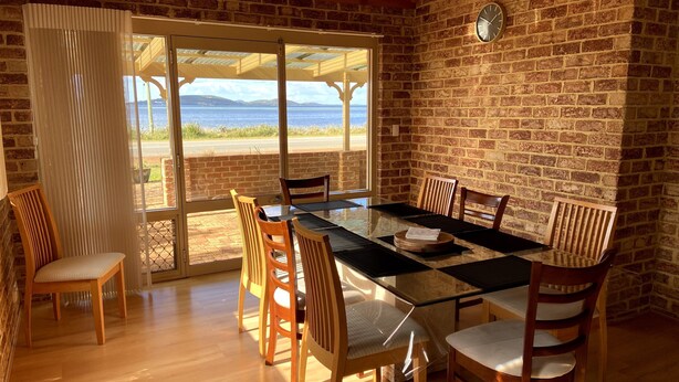 A dining area with a glass table and wooden chairs, a brick wall, and a view of the sea. - Enjoy Sunrise Views from the comfort of this beautiful home away from home! (Little Grove)
