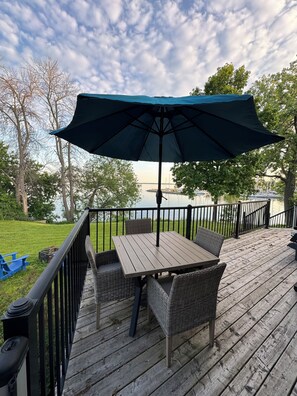 A wooden deck with a table and chairs, a large umbrella, and a view of the water. - Gorgeous Waterfront home with sweeping views of a beautiful bay. (Bath)