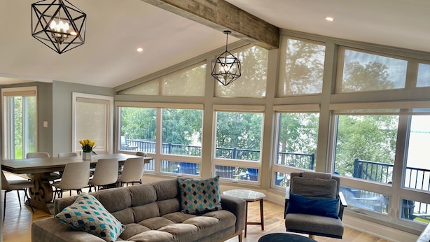 A spacious living room with a large sofa, ottomans, and a dining area with chairs and a table. - Gorgeous Waterfront home with sweeping views of a beautiful bay. (Bath)