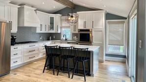 A modern kitchen with white cabinets, a central island with bar stools, stainless steel appliances, and a unique geometric light fixture. - Gorgeous Waterfront home with sweeping views of a beautiful bay. (Bath)