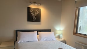 A neatly made bed with white linens, a headboard, and a wall-mounted artwork of a deer head.