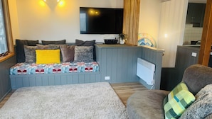 A compact living space with a sofa, a small table, a television, and a kitchen area.