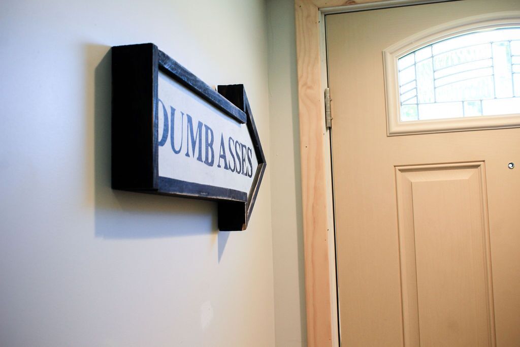 A sign on a wall that reads "DUMB ASSES" with an arrow pointing to the right.