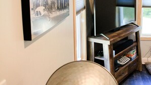 En stue med et stort fladskærms-tv, et underholdningscenter i vintage-stil, og et indrammet historisk fotografi på væggen.