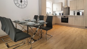 A modern kitchen with wooden cabinets, a built-in oven, and a dining area with a glass table and black chairs. - Sea Nest (Torquay)