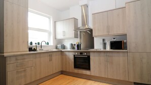 A modern kitchen with light wood cabinets, a stainless steel range hood, a built-in oven, and a microwave. - Sea Nest (Torquay)