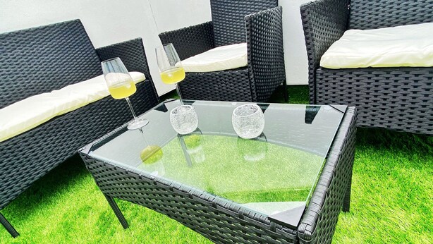 A glass-top table with wicker chairs and cushions, surrounded by artificial green grass. - Sea Nest (Torquay)