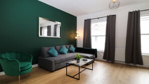 A modern living room with a dark green wall, a grey sofa with teal cushions, a green armchair, and a coffee table with a plant. - Sea Nest (Torquay)