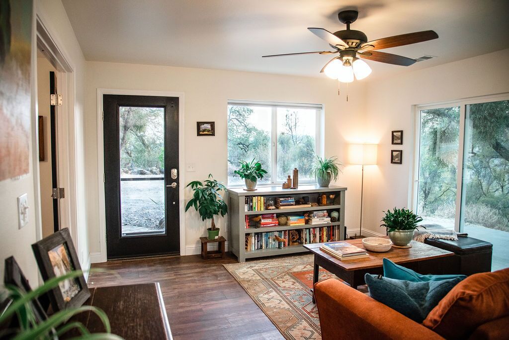 A cozy living room with a dark wooden floor, a bookshelf, a sofa, and a ceiling fan.
