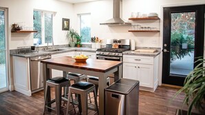 Een moderne keuken met een centraal kookeiland, roestvrijstalen apparatuur en een zwarte deur met uitzicht op groen.