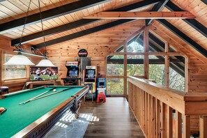 A wooden interior with a pool table, arcade games, and large windows. - Located Directly Between Gatlinburg & Pigeon Forge -EV Chrgr🚙🪫🔌-Amazing Reviews🏅 (Gatlinburg)