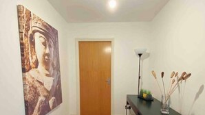 A hallway with wooden flooring, a Buddha statue, a door, a desk with a lamp, and a black shelf with items. - The OVO Hydro Penthouse With Free Parking (Glasgow)