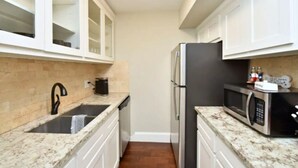 Una cocina compacta con armarios blancos, un refrigerador de acero inoxidable, un microondas y un lavamanos con grifo.