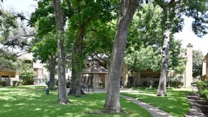 Un patio con un pabellón, rodeado de árboles y un edificio con fachada de piedra.