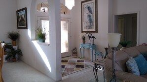 A spacious living room with a large window, a chandelier, and a blue side table with decorative items. - Book this home for a relaxing vacation in Rotonda West! (Rotonda West)