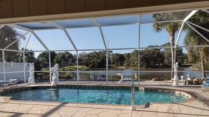 A covered swimming pool with statues, a view of a lake, and a patio area. - Book this home for a relaxing vacation in Rotonda West! (Rotonda West)