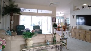 A spacious living room with a beige sofa, a coffee table, and a TV mounted on the wall. - Book this home for a relaxing vacation in Rotonda West! (Rotonda West)