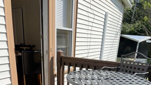 Un patio con sillas y una mesa de metal, una puerta que da a una habitación y una pared exterior blanca.