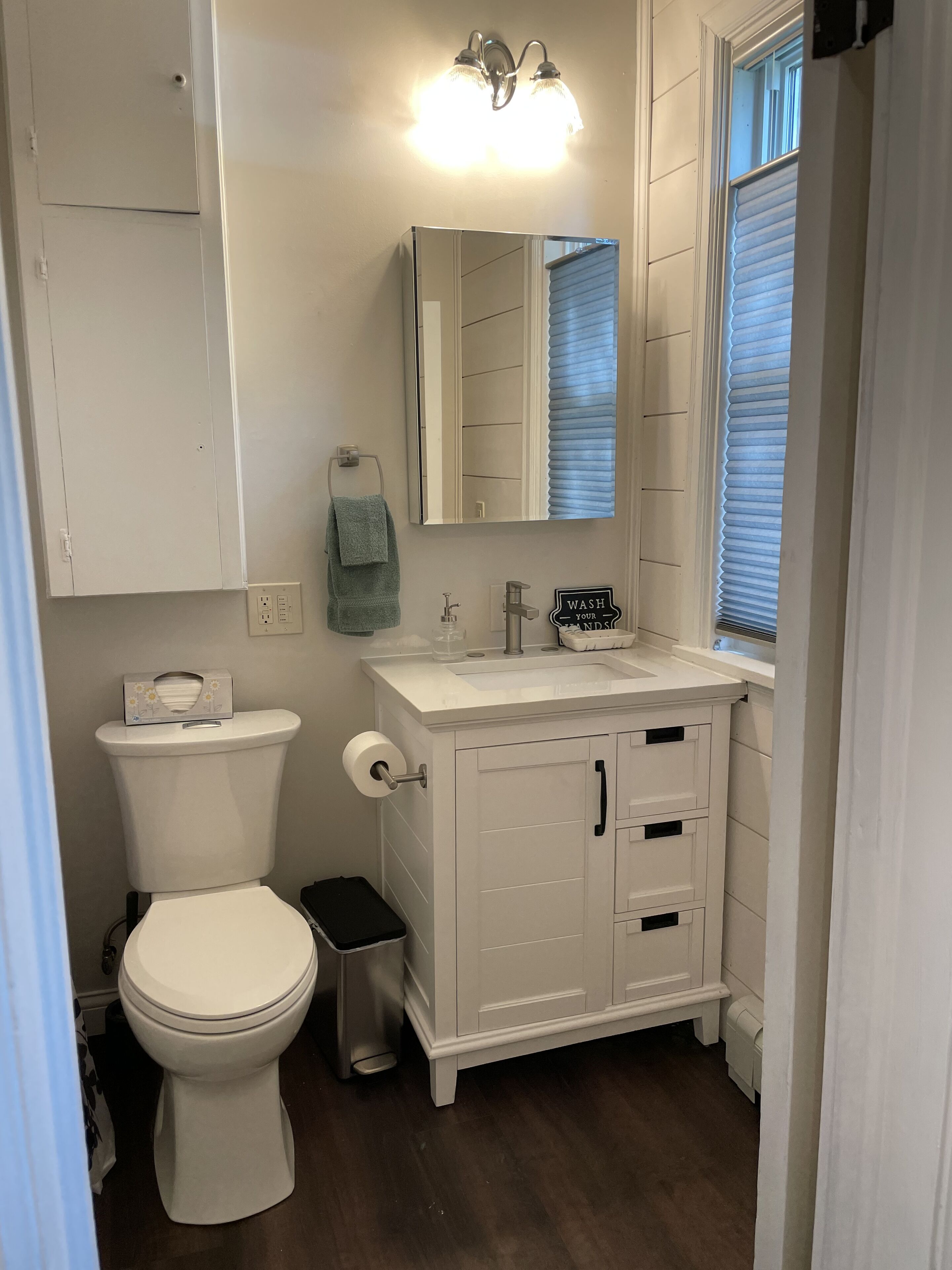 A bathroom with a toilet, sink, mirror, and cabinet.