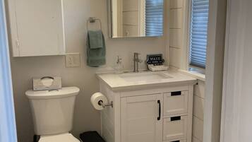 A bathroom with a toilet, sink, mirror, and cabinet.