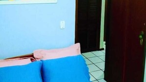 Une pièce avec un lit, un oreiller bleu et rose, un sol carrelé et une porte en bois.