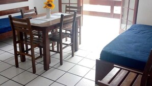 Une pièce comprenant une table à manger en bois, quatre chaises, un vase avec des tournesols et un lit recouvert d’une couverture bleue.