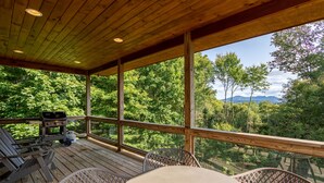 A wooden deck with a table and chairs, overlooking a forested area with mountains in the distance. - Shady Pines - modern mountain home near winery, game table, fire pit (Banner Elk)