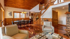 A spacious living area with wooden floors, a dining table, and a staircase leading to an upper level. - Shady Pines - modern mountain home near winery, game table, fire pit (Banner Elk)