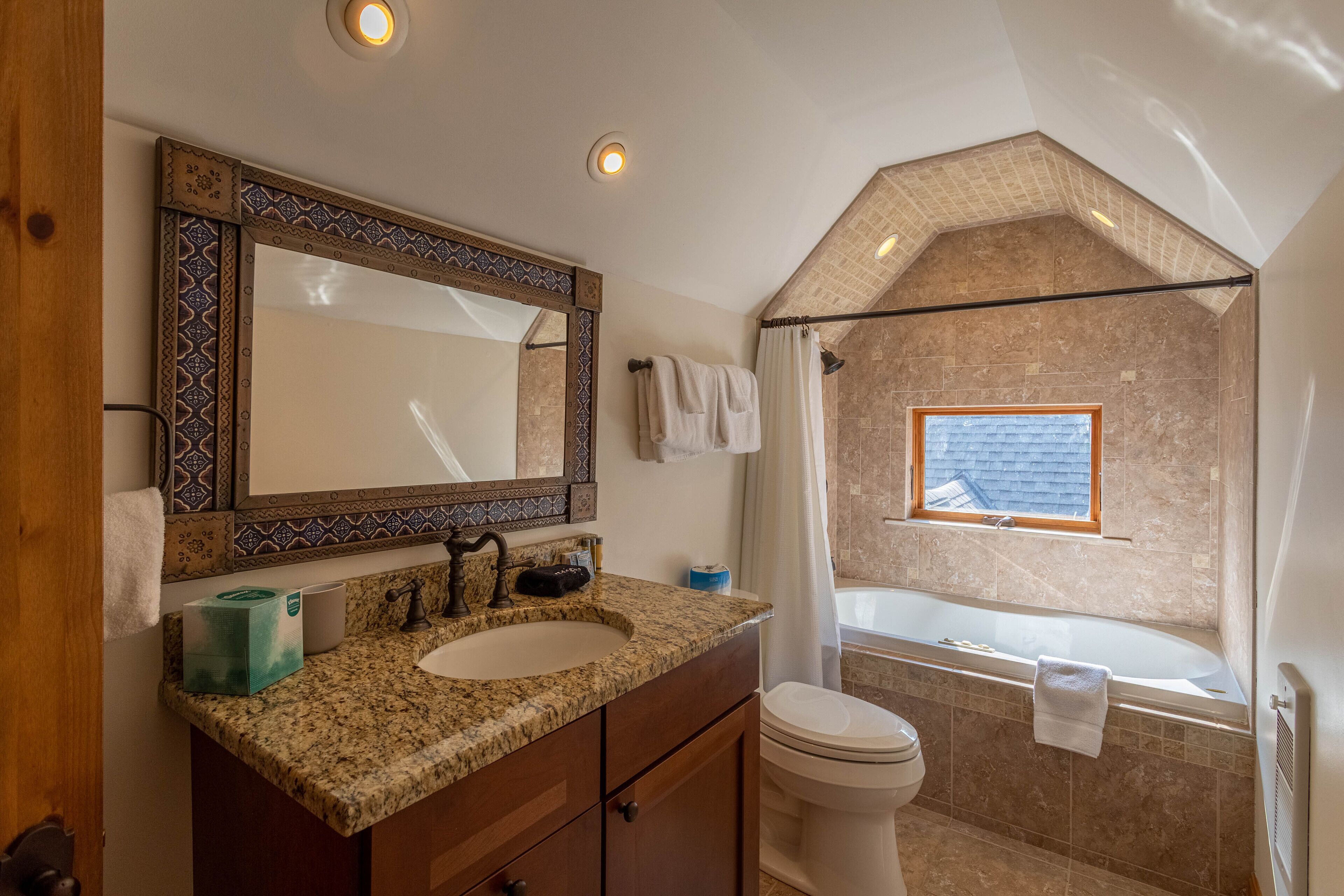 A bathroom with a sink, mirror, and toilet. There is a window with a view of the outside.