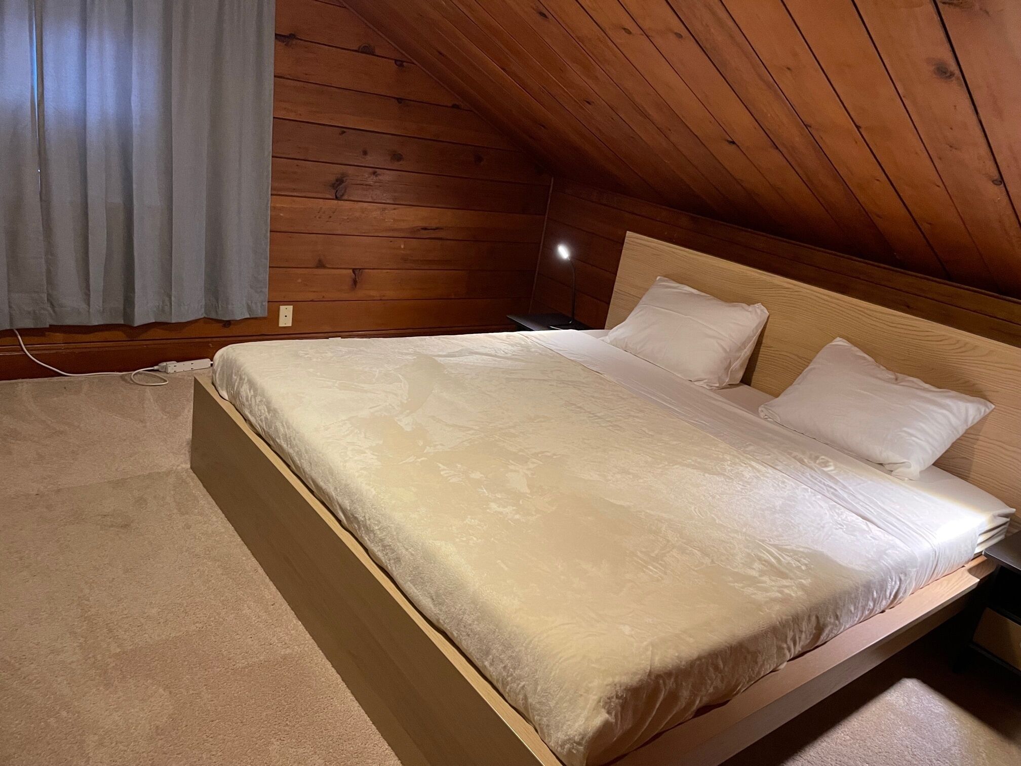 Un dormitorio con techo de madera, una cama con ropa blanca y una mesita de noche.