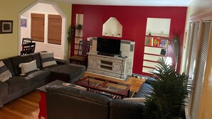 A living room with a large sectional sofa, a television on a white cabinet, and a red accent wall. - Olympic Hills six bed haven with hot tub and grill (Seattle)