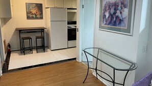 A compact kitchen with a refrigerator, stove, and a small dining table with stools. There are two framed floral paintings on the walls. - Olympic Hills six bed haven with hot tub and grill (Seattle)