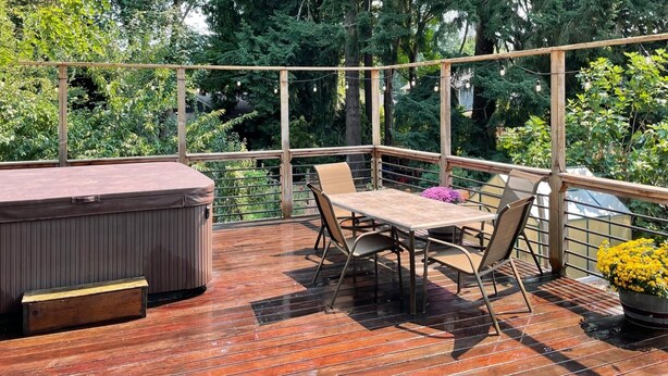 A wooden deck with a hot tub, a table with chairs, and potted plants. - Olympic Hills six bed haven with hot tub and grill (Seattle)