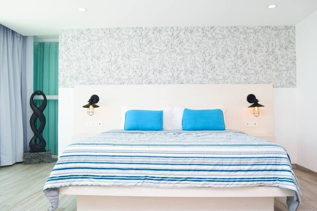 Una camera da letto moderna con un letto grande, due cuscini blu e due lampade da lettura fissate al muro.