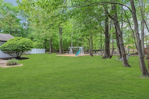 A backyard with a swing set, a small tree, and a grassy lawn.